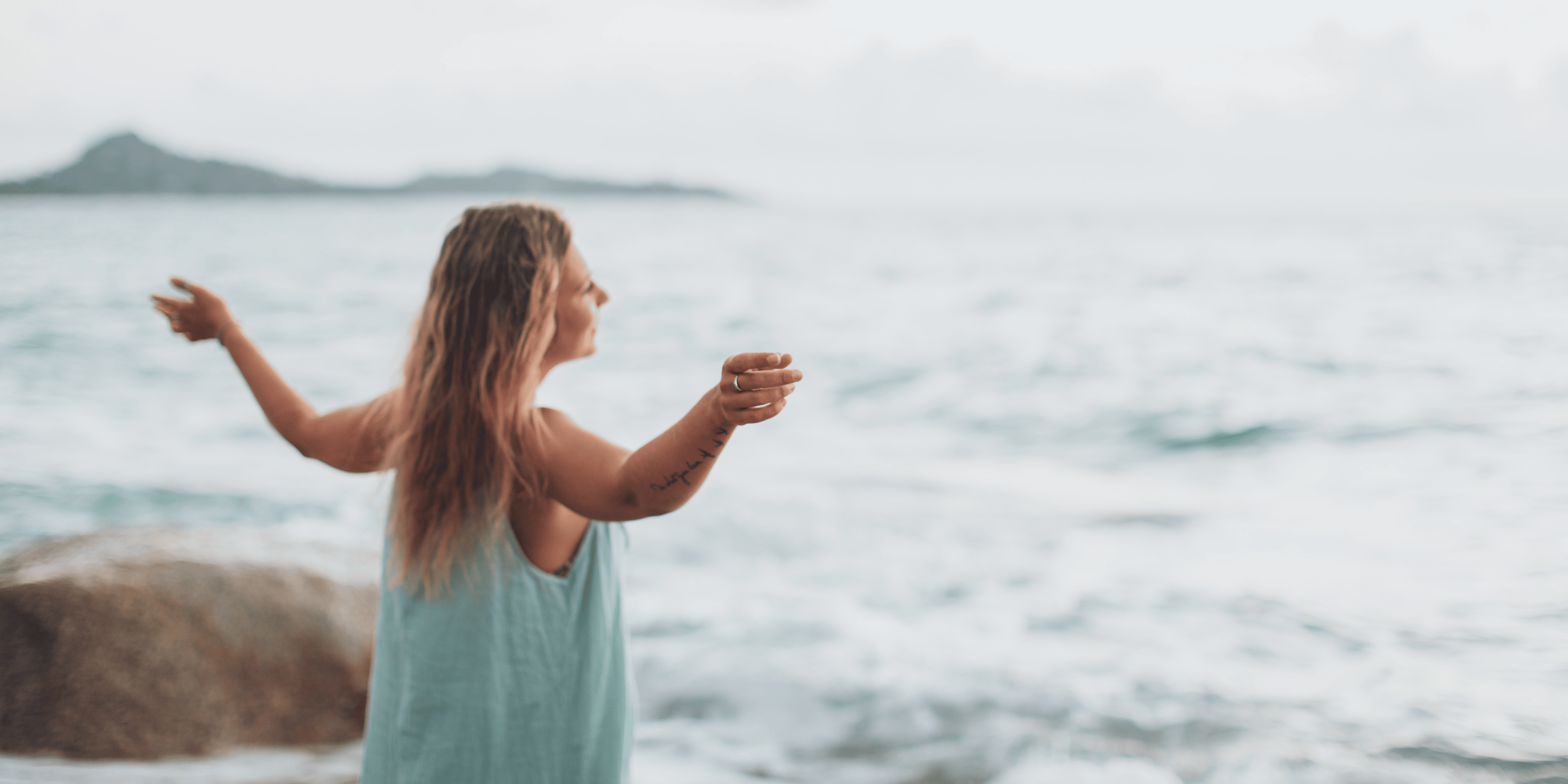 A woman standing by the sea, raising her arms to breathe in the fresh air, finding a moment of relaxation and peace İn the name of motherhood